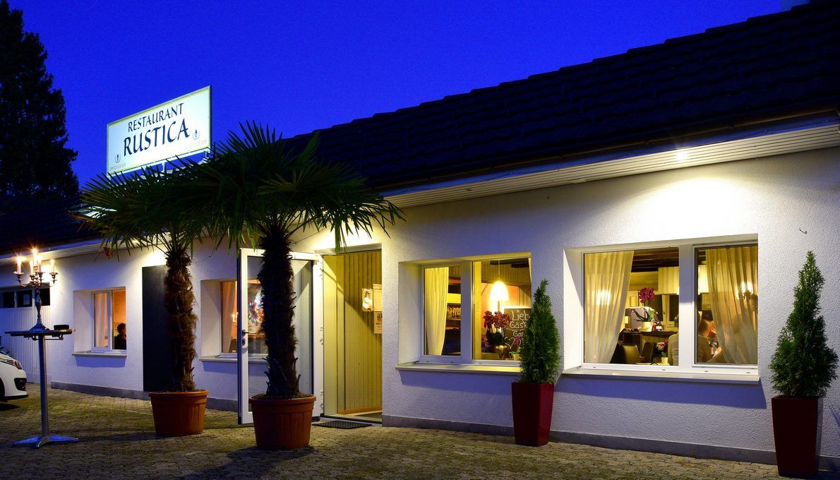 Restaurant Rustica am Abend mit beleuchtetem Schild beim Eingang